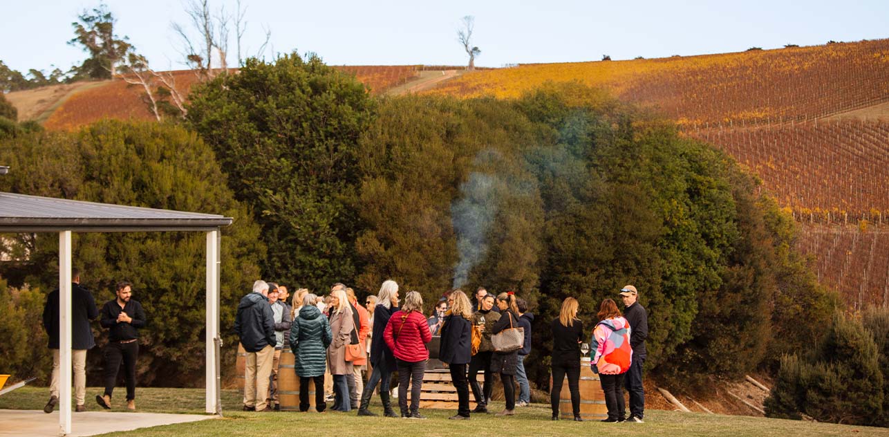 A group of people gathered outdoors at a wine event in a scenic vineyard setting